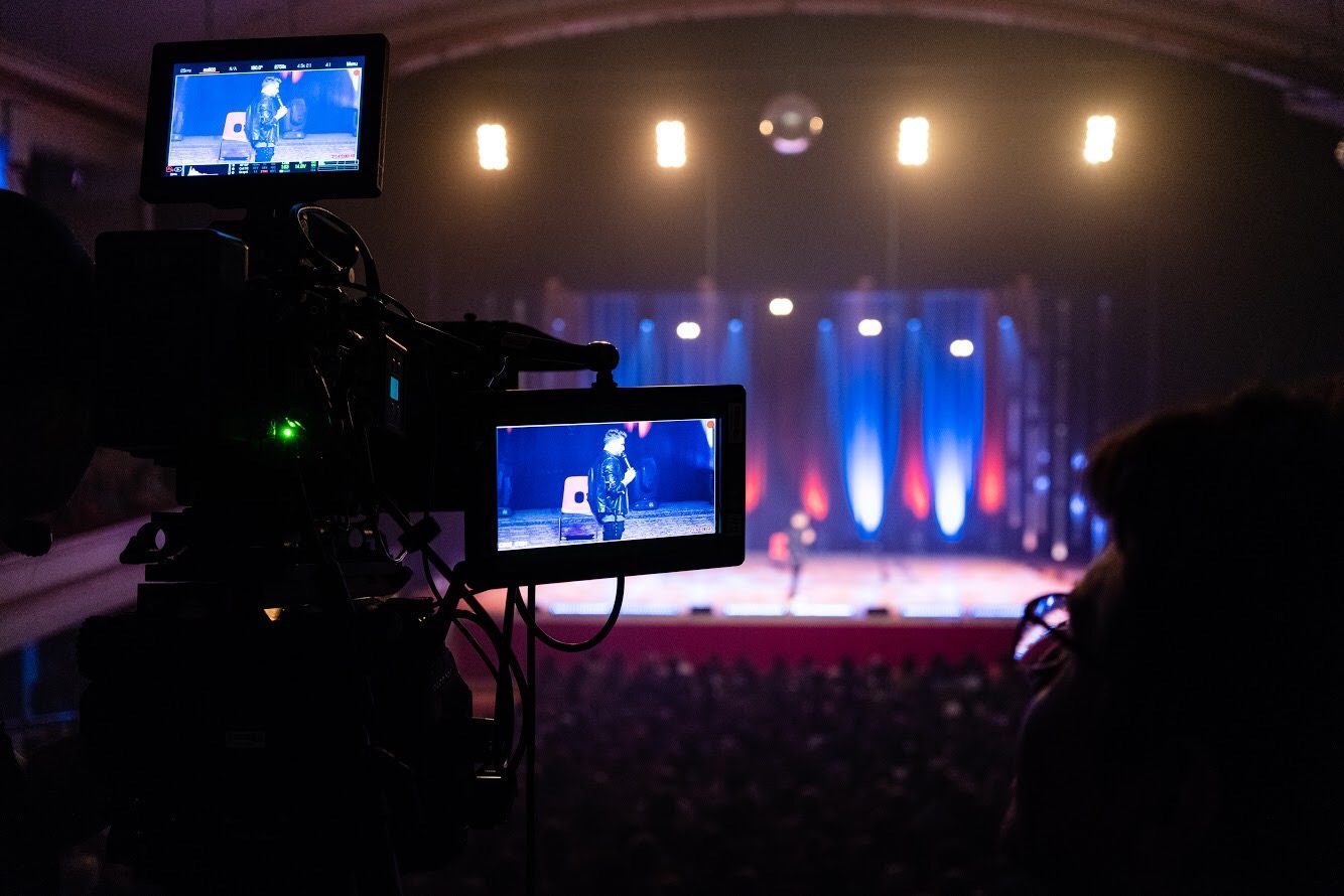 Camera monitors framing a comedian on stage during a live theatre recording