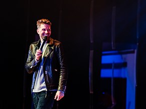 Comedian smiling on stage under blue light