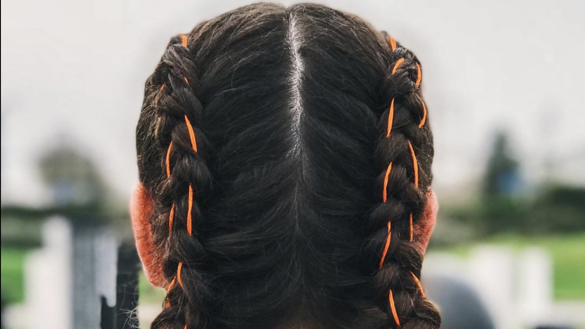 A woman with orange-threaded braids seen from behind